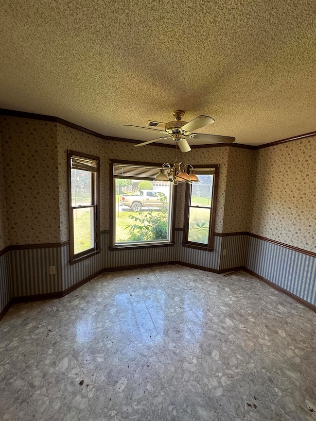Spare room featuring a textured ceiling, ornamental molding, a ceiling fan, and wallpapered walls