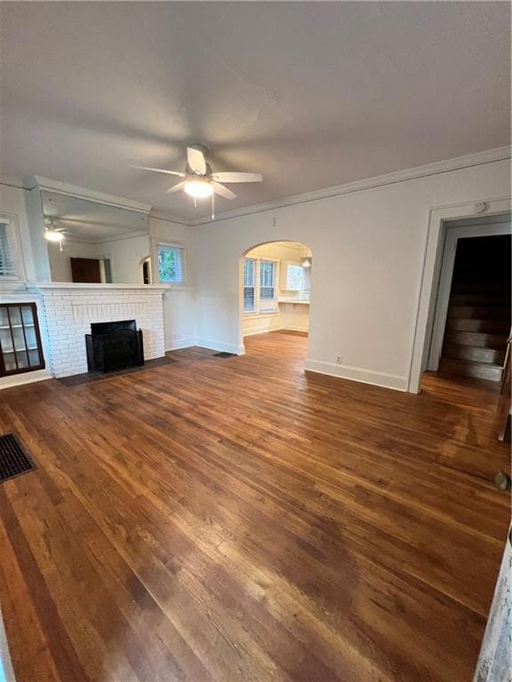 Unfurnished living room featuring crown molding, a fireplace, arched walkways, dark wood-style flooring, and stairs