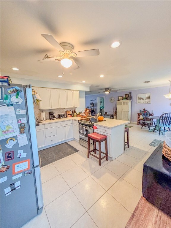 Kitchen featuring a peninsula, stainless steel appliances, a breakfast bar area, white cabinets, and light countertops