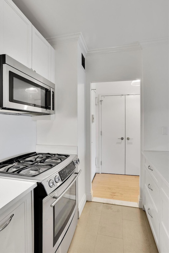 Kitchen featuring stainless steel appliances, light countertops, ornamental molding, white cabinets, and light flooring