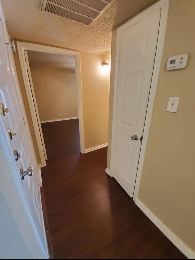 Corridor with dark wood-style floors, visible vent