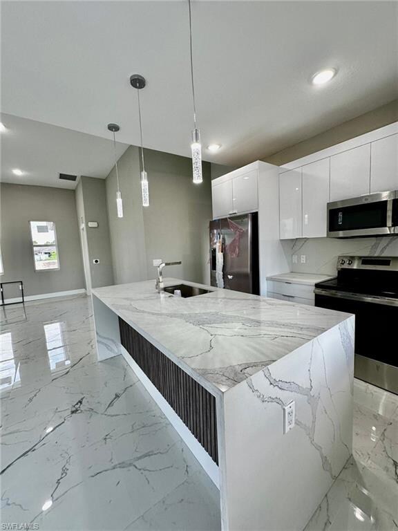 Kitchen with decorative light fixtures, sink, white cabinets, stainless steel appliances, and a center island with sink