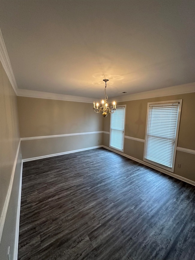 Spare room with crown molding, a chandelier, and dark wood-style floors