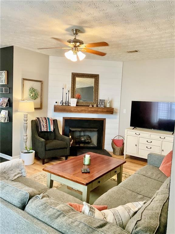 Living room with light wood finished floors, a textured ceiling, a ceiling fan, and a fireplace