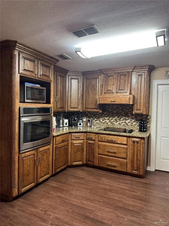 Kitchen featuring stainless steel appliances, decorative backsplash, dark wood-style flooring, a textured ceiling, and brown cabinetry