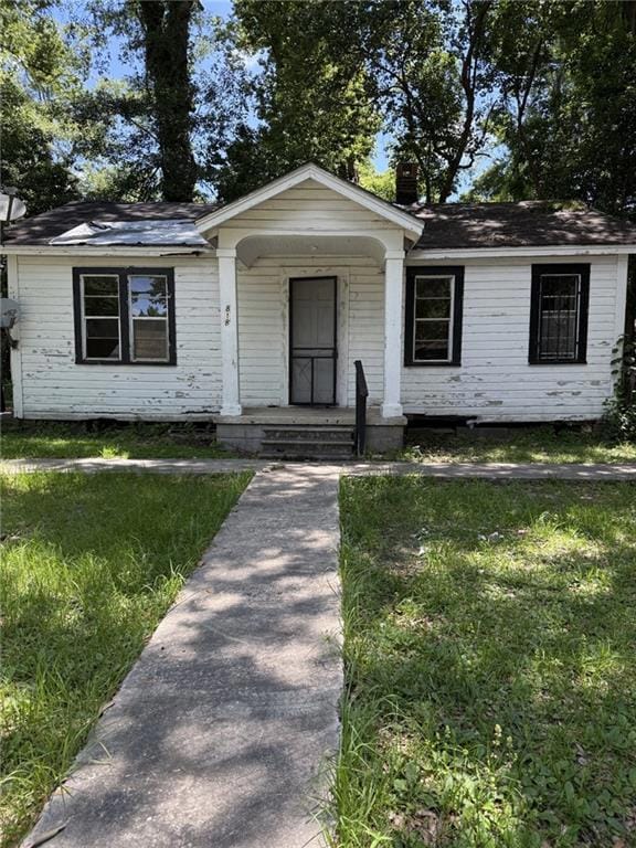 View of front facade with covered porch, a chimney, a shingled roof, and a front yard