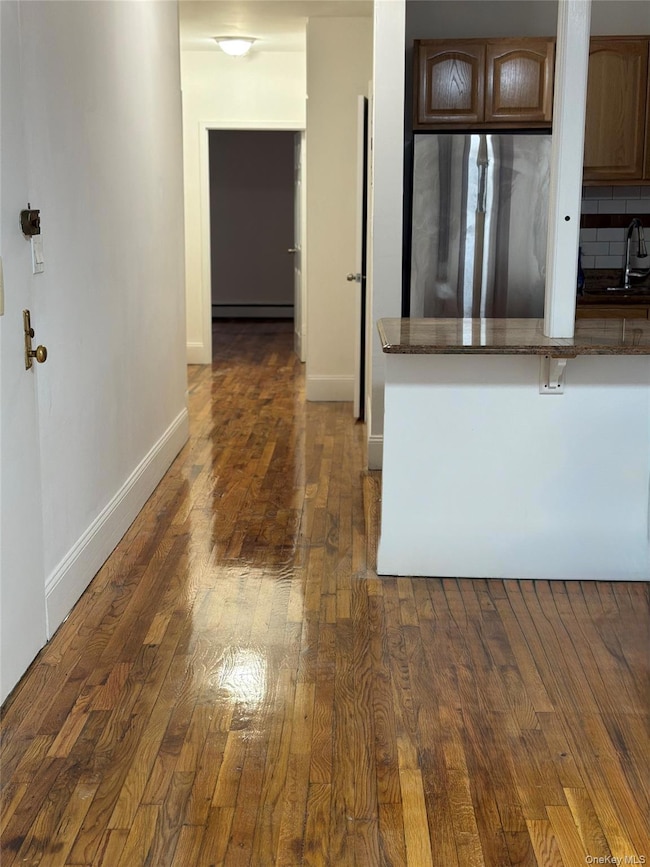 Kitchen featuring stainless steel fridge, dark wood-style flooring, light stone counters, tasteful backsplash, and a breakfast bar