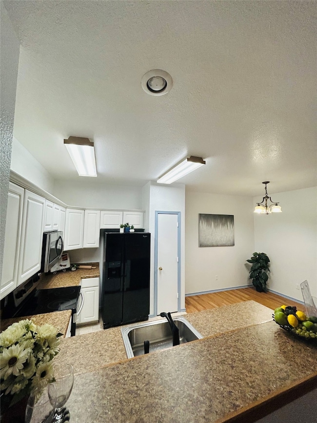 Kitchen with white cabinets, decorative light fixtures, a textured ceiling, stainless steel appliances, and light wood-style floors