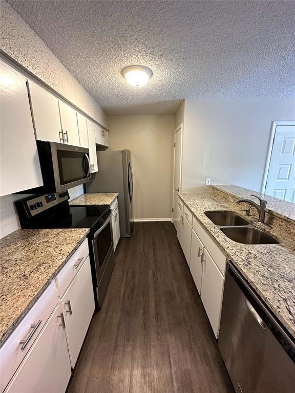 Kitchen with appliances with stainless steel finishes, light stone countertops, dark wood finished floors, a textured ceiling, and white cabinets