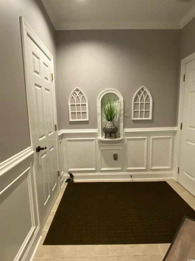 Entryway with a decorative wall, tile patterned flooring, a wainscoted wall, crown molding, and elevator