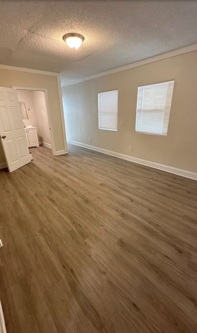 Unfurnished bedroom with crown molding, a textured ceiling, and dark wood-type flooring