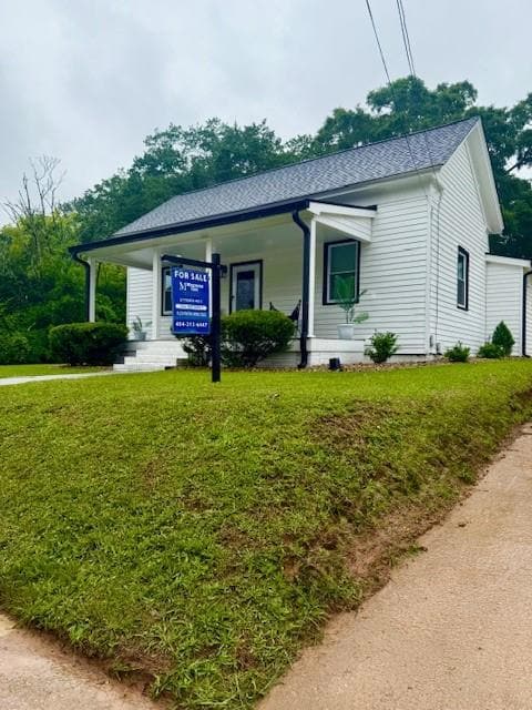 View of front of house with covered porch, a front yard, and a shingled roof