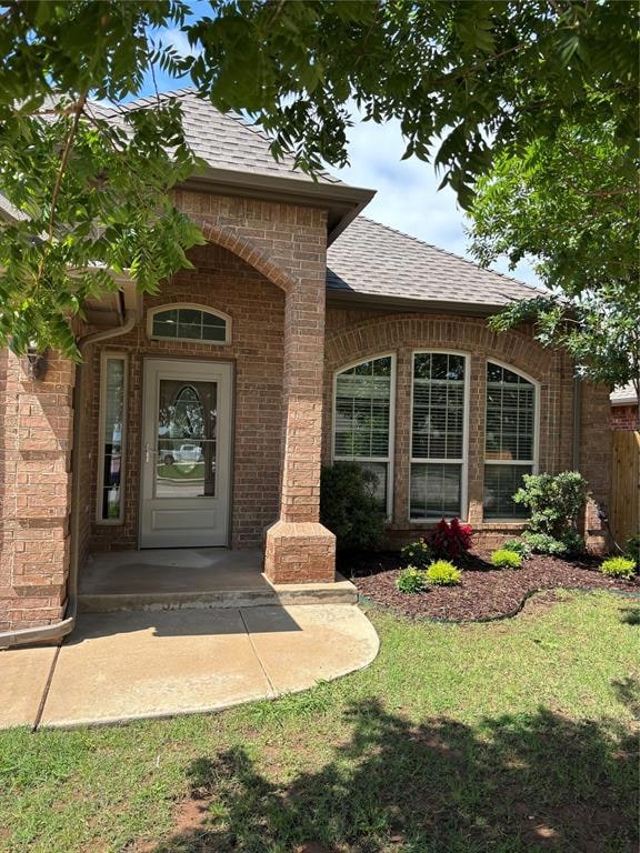 Entrance to property featuring roof with shingles and brick siding