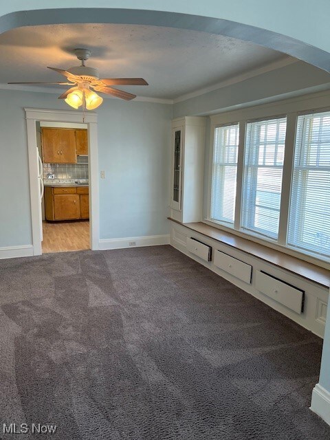Carpeted empty room featuring crown molding, ceiling fan, and a wealth of natural light