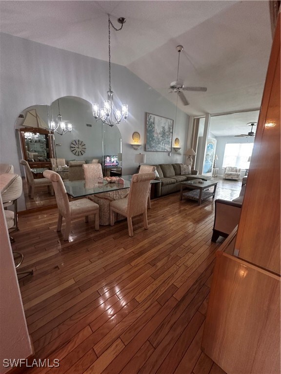Living area featuring a ceiling fan, wood-type flooring, a chandelier, arched walkways, and vaulted ceiling