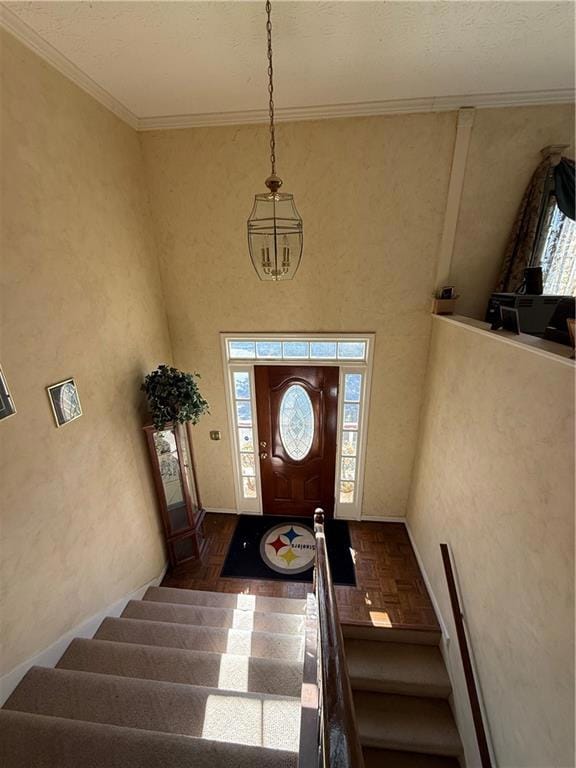 Foyer with stairway, ornamental molding, a towering ceiling, parquet floors, and a chandelier