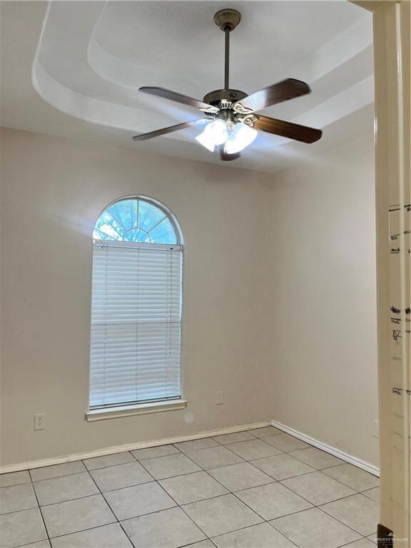 Unfurnished room featuring light tile floors, a raised ceiling, and ceiling fan