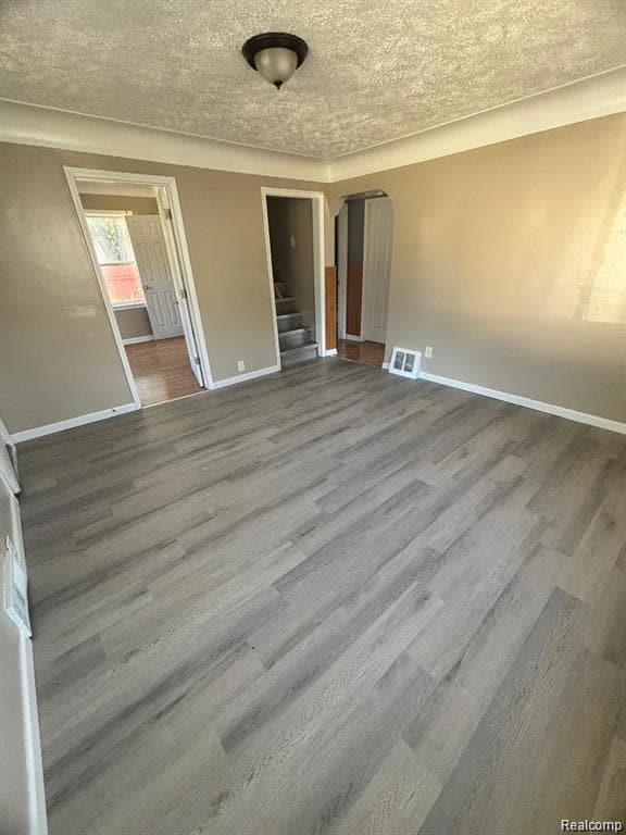 Unfurnished bedroom featuring wood finished floors, arched walkways, and a textured ceiling