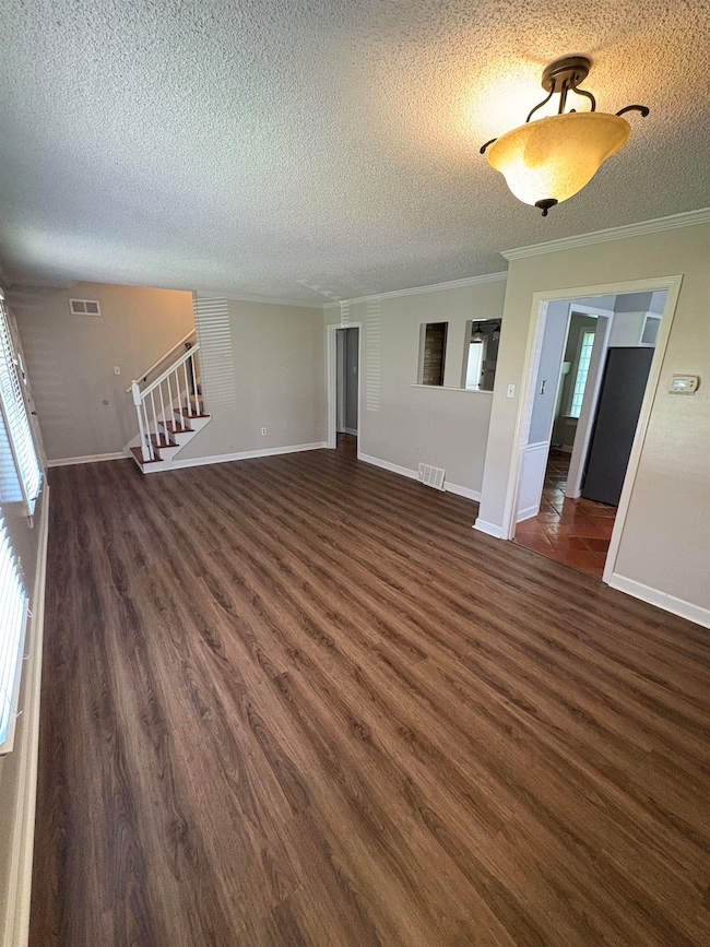 Unfurnished living room featuring a textured ceiling, crown molding, dark wood finished floors, and stairs