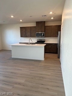 Kitchen featuring dark brown cabinets, light wood-style flooring, light countertops, an island with sink, and recessed lighting