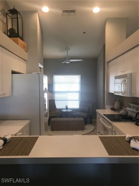 Kitchen with a ceiling fan, white cabinetry, fridg