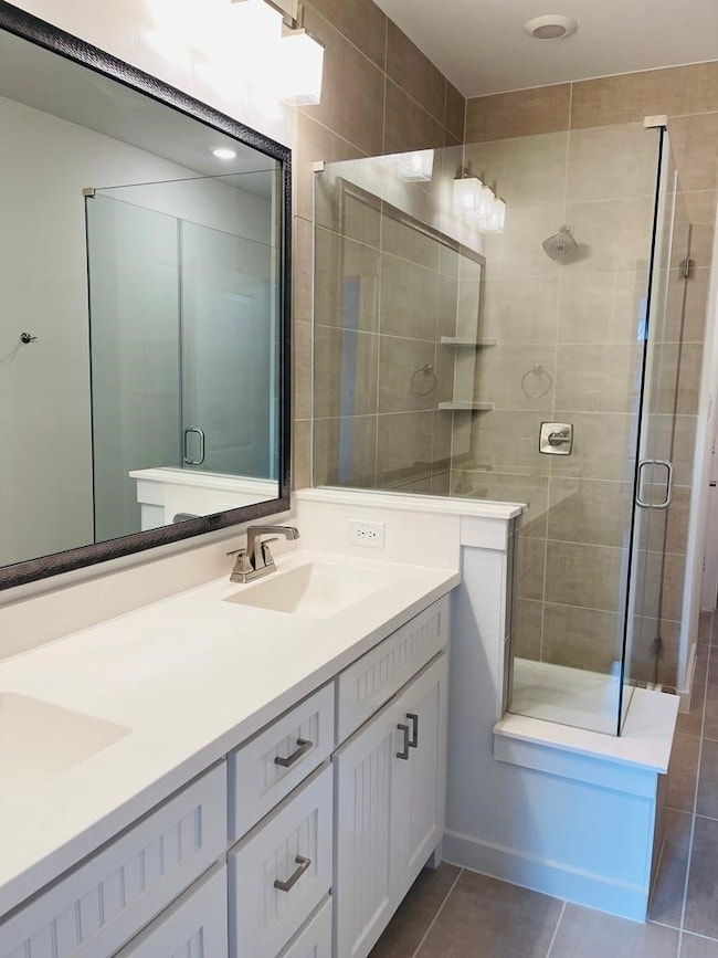 Bathroom with double vanity, dark tile patterned floors, and a stall shower