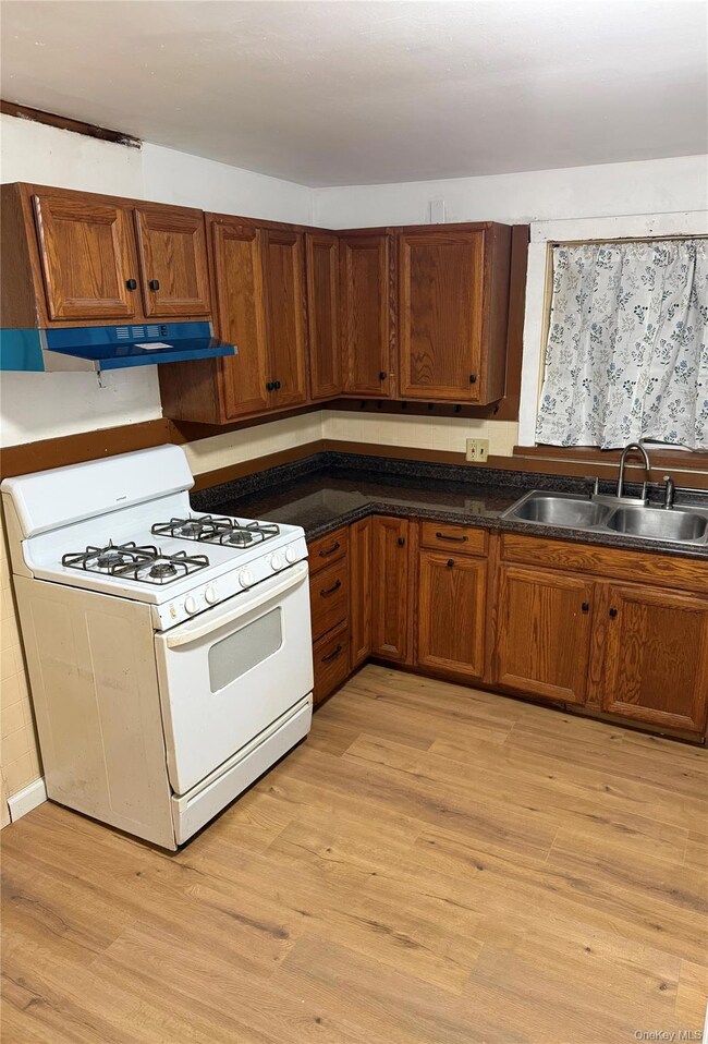 Kitchen with white gas range oven, dark countertops, brown cabinetry, and light wood finished floors