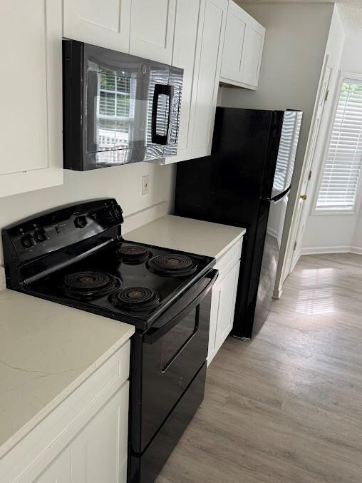 Kitchen with black appliances, white cabinets, light wood-style flooring, and light stone countertops