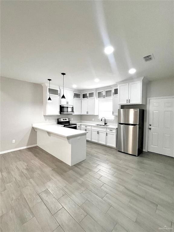 Kitchen featuring a peninsula, light countertops, hanging light fixtures, light wood-type flooring, and appliances with stainless steel finishes