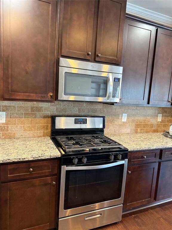 Kitchen with stainless steel appliances, dark brown cabinetry, light stone countertops, and crown molding