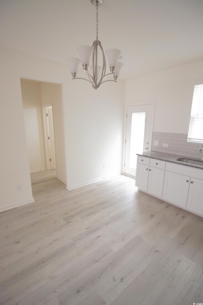 Unfurnished dining area with a sink, a chandelier, light wood-type flooring, and baseboards