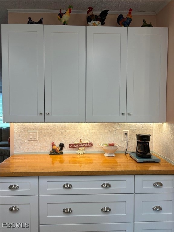 Kitchen featuring wood counters, tasteful backsplash, white cabinetry, a textured ceiling, and ornamental molding