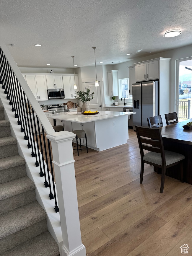 Kitchen with appliances with stainless steel finishes, healthy amount of natural light, a textured ceiling, a kitchen island, and light wood-style floors