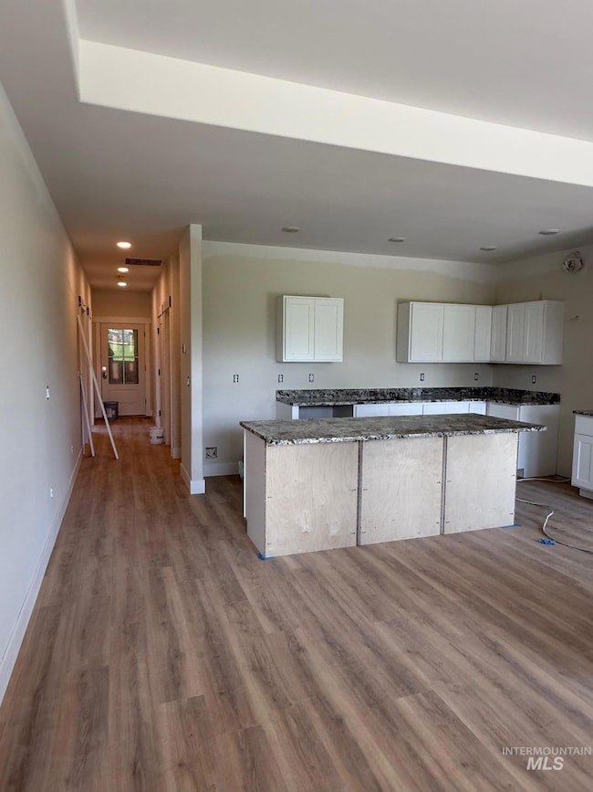 Kitchen with white cabinets, wood finished floors, dark stone counters, a kitchen island, and recessed lighting