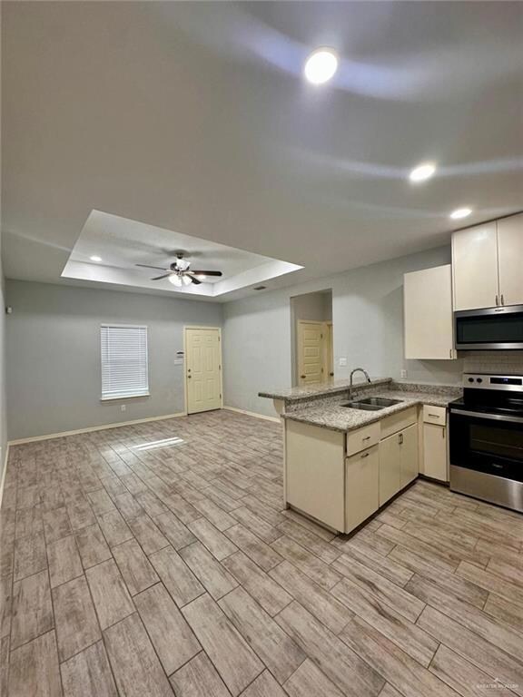 Kitchen with a tray ceiling, stainless steel appliances, a peninsula, wood tiled floors, and recessed lighting