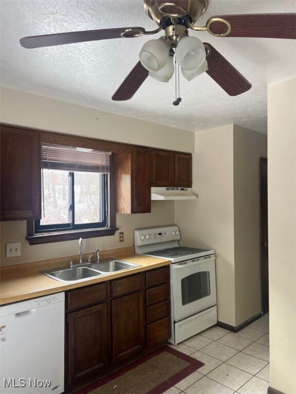 Kitchen featuring white appliances, light tile patterned floors, sink, a textured ceiling, and dark brown cabinetry