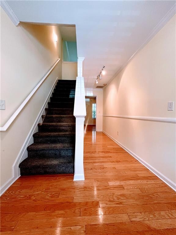 Staircase with baseboards, rail lighting, hardwood