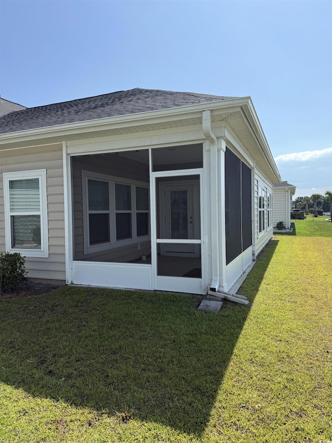 View of side of home with a shingled roof, a lawn, and a sunroom