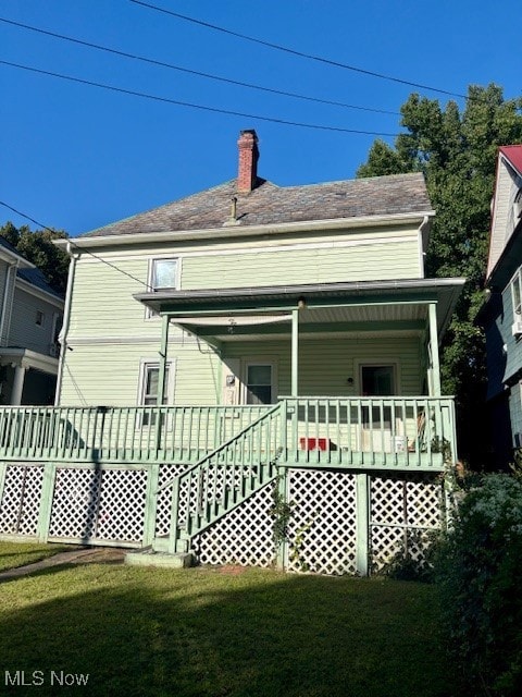 Back of house with a chimney, a lawn, and covered porch