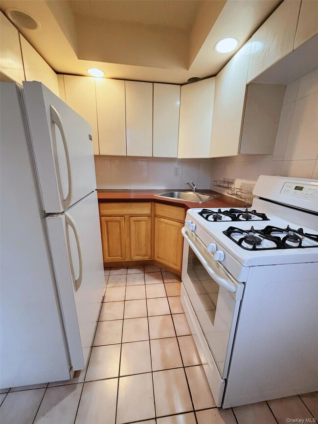 Kitchen with white appliances, light tile patterned flooring, decorative backsplash, recessed lighting, and light countertops