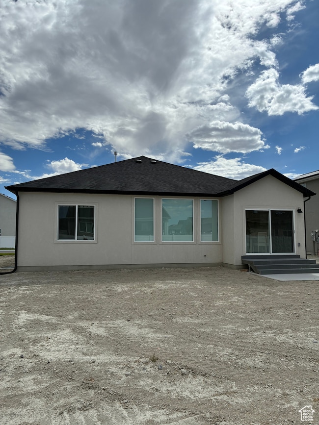 Back of house featuring a shingled roof and stucco siding