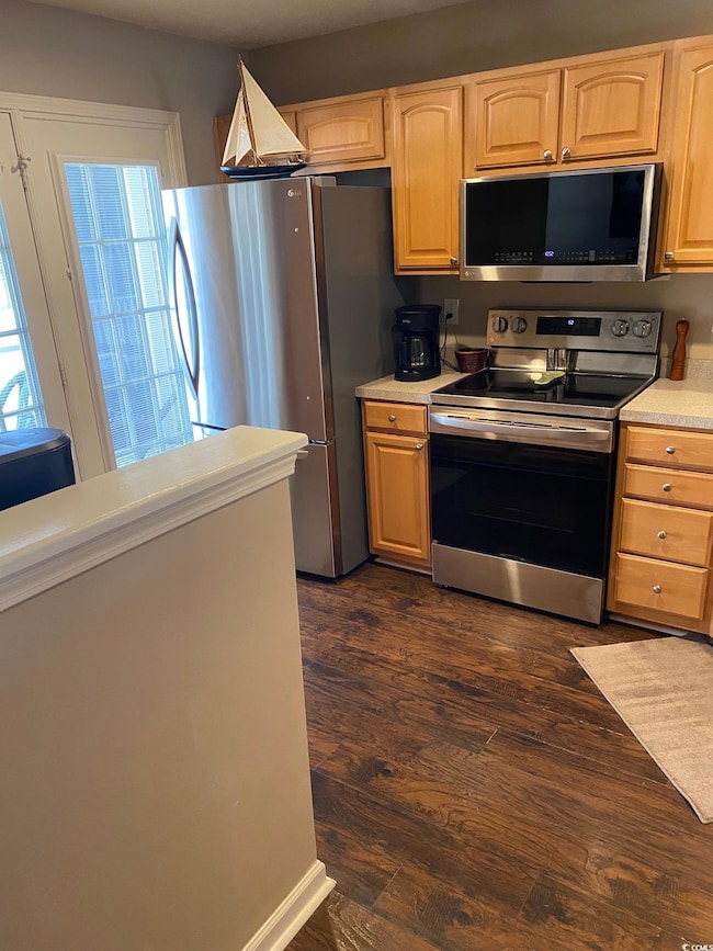 Kitchen with stainless steel appliances, light countertops, dark wood-style floors, and light brown cabinetry