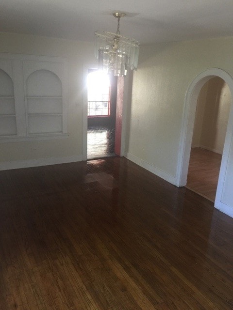 Empty room featuring built in shelves, dark wood-style floors, and arched walkways