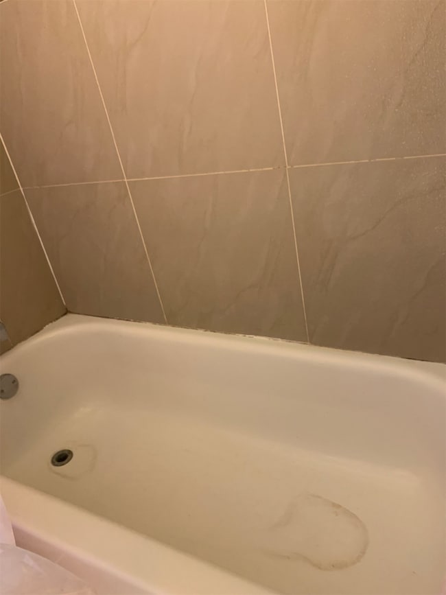 The photo shows a standard white bathtub with beig