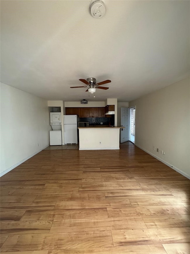 Unfurnished living room featuring light wood-style floors, stacked washing machine and dryer, and a ceiling fan