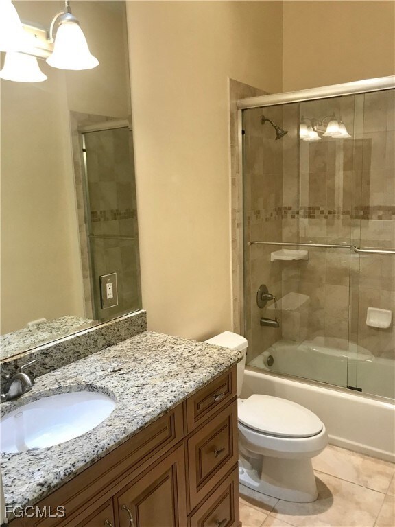 Full guest bathroom with combined bath / shower with glass door, vanity, and light tile patterned flooring