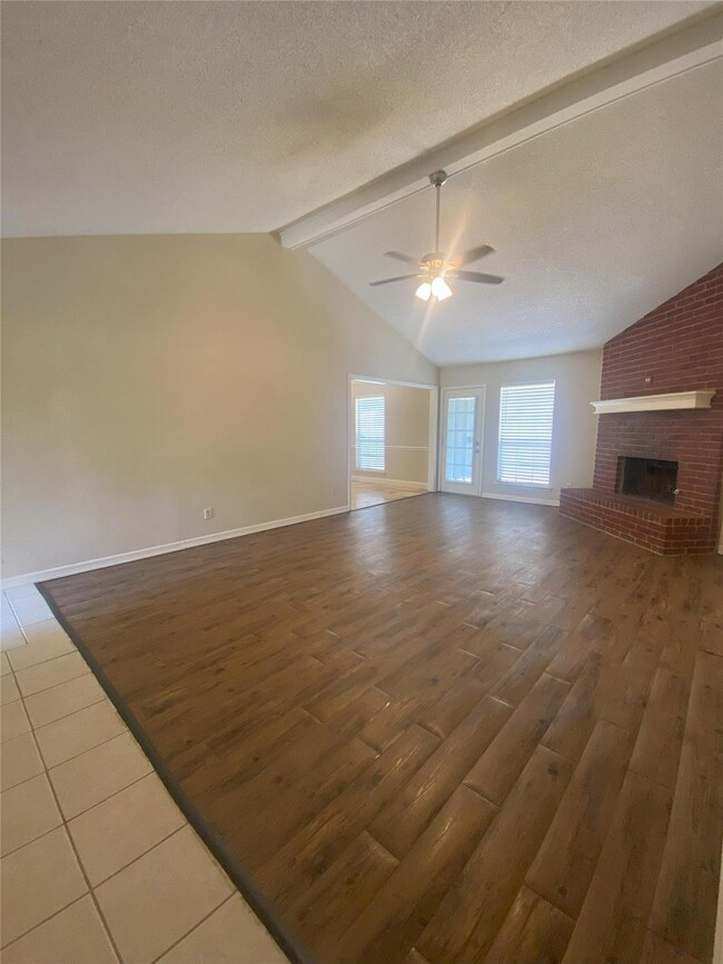 Unfurnished living room with ceiling fan, a brick fireplace, vaulted ceiling with beams, wood-type flooring, and a textured ceiling