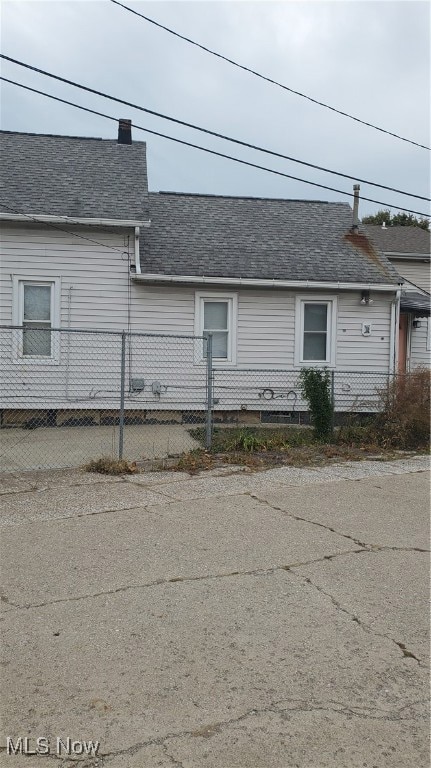 View of side of home with roof with shingles, a fenced front yard, and a chimney