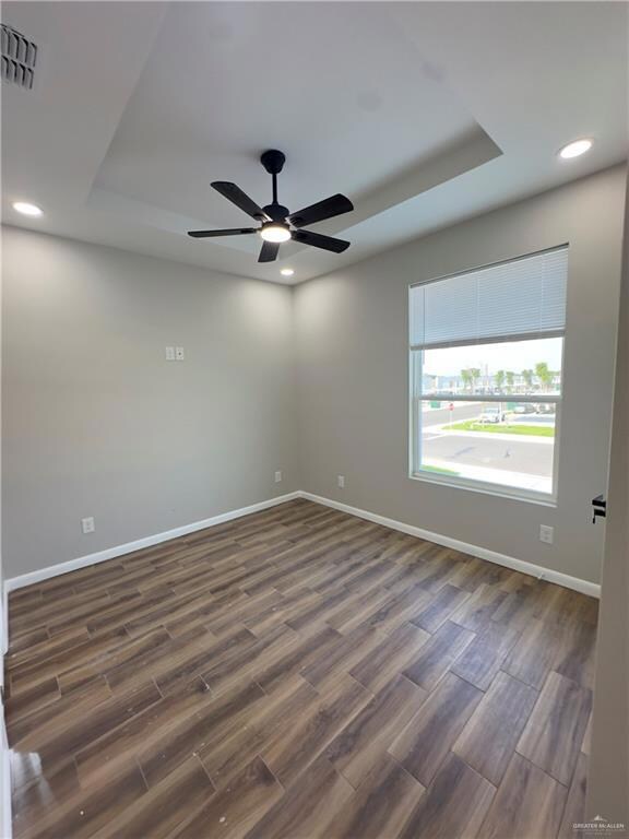 Empty room with a raised ceiling, baseboards, dark wood-style flooring, recessed lighting, and ceiling fan