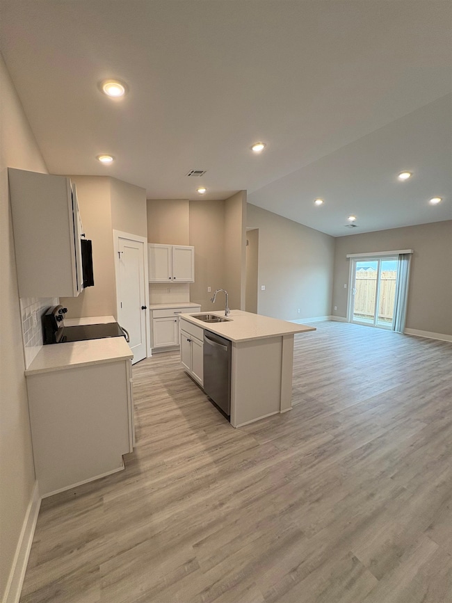 Kitchen with open floor plan, recessed lighting, light wood finished floors, white cabinets, and a center island with sink